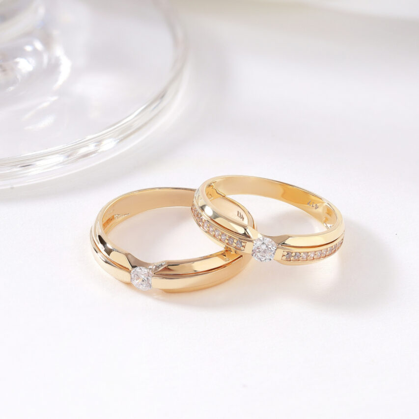 Cặp nhẫn cưới vàng mang thiết kế tinh giản nhưng tinh tế, điểm nhấn là viên đá CZ nổi bật ở giữa, tượng trưng cho trái tim chung thủy và sáng rõ.