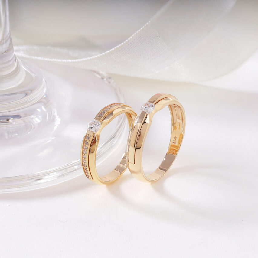 Cặp nhẫn cưới vàng mang thiết kế tinh giản nhưng tinh tế, điểm nhấn là viên đá CZ nổi bật ở giữa, tượng trưng cho trái tim chung thủy và sáng rõ.